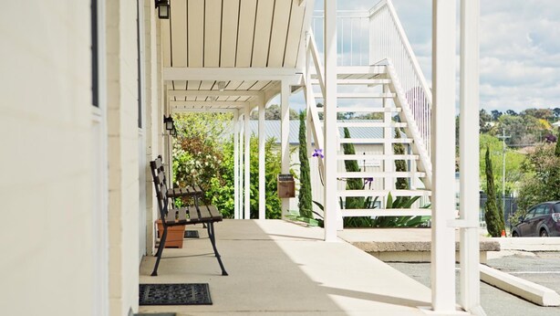 A covered porch with a wooden bench, a white staircase, and a view of the surrounding greenery. - Colonial Lodge Motor Inn Yass (Yass)