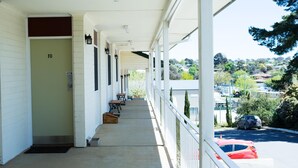 A motel with a covered porch, numbered room 10, outdoor seating, and a view of a parking lot and greenery. - Colonial Lodge Motor Inn Yass (Yass)