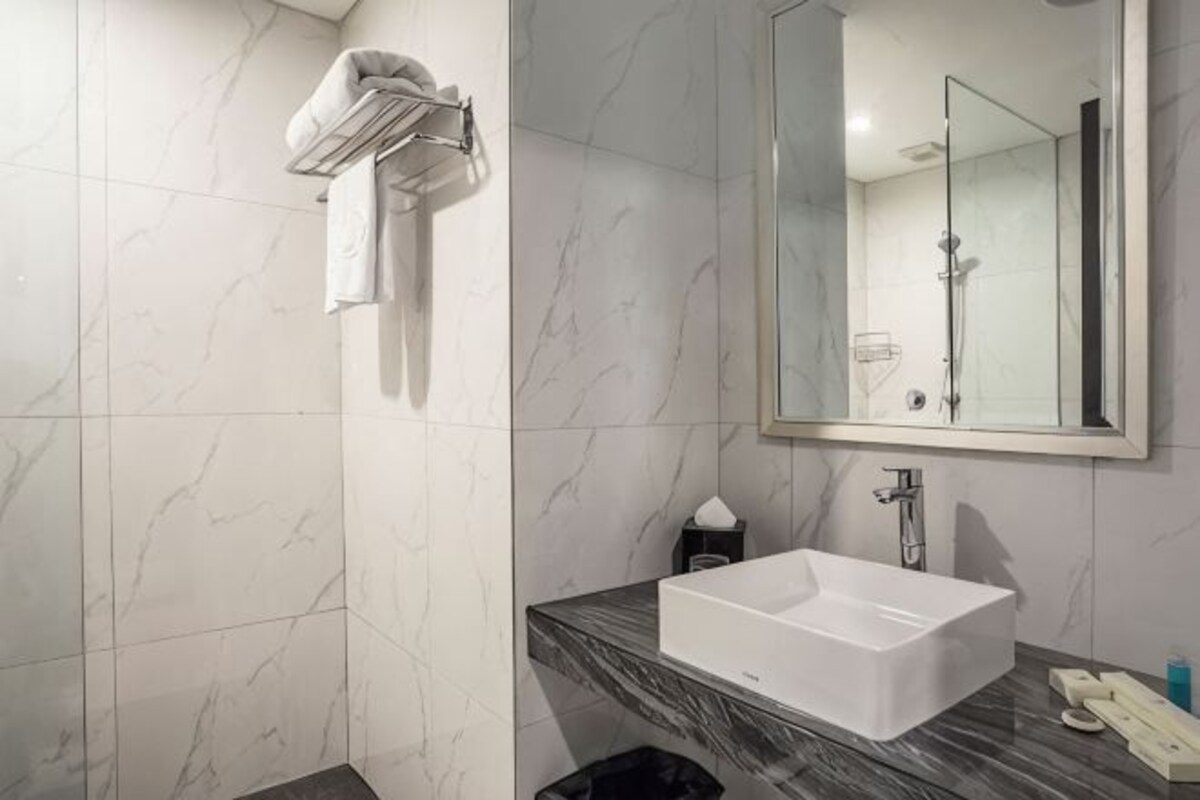 Un baño con pared de mármol, un lavamanos blanco, un espejo y un perchero para toallas.