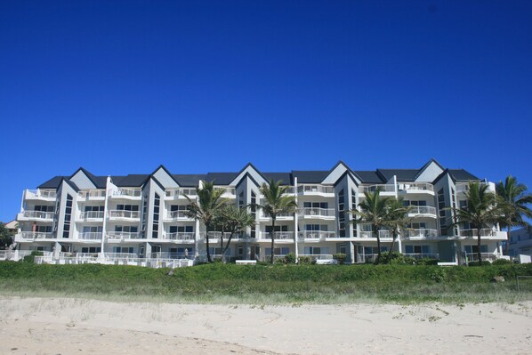 Un hôtel situé en bord de mer, doté de nombreux balcons, de palmiers et offrant une vue sur un ciel bleu azur.