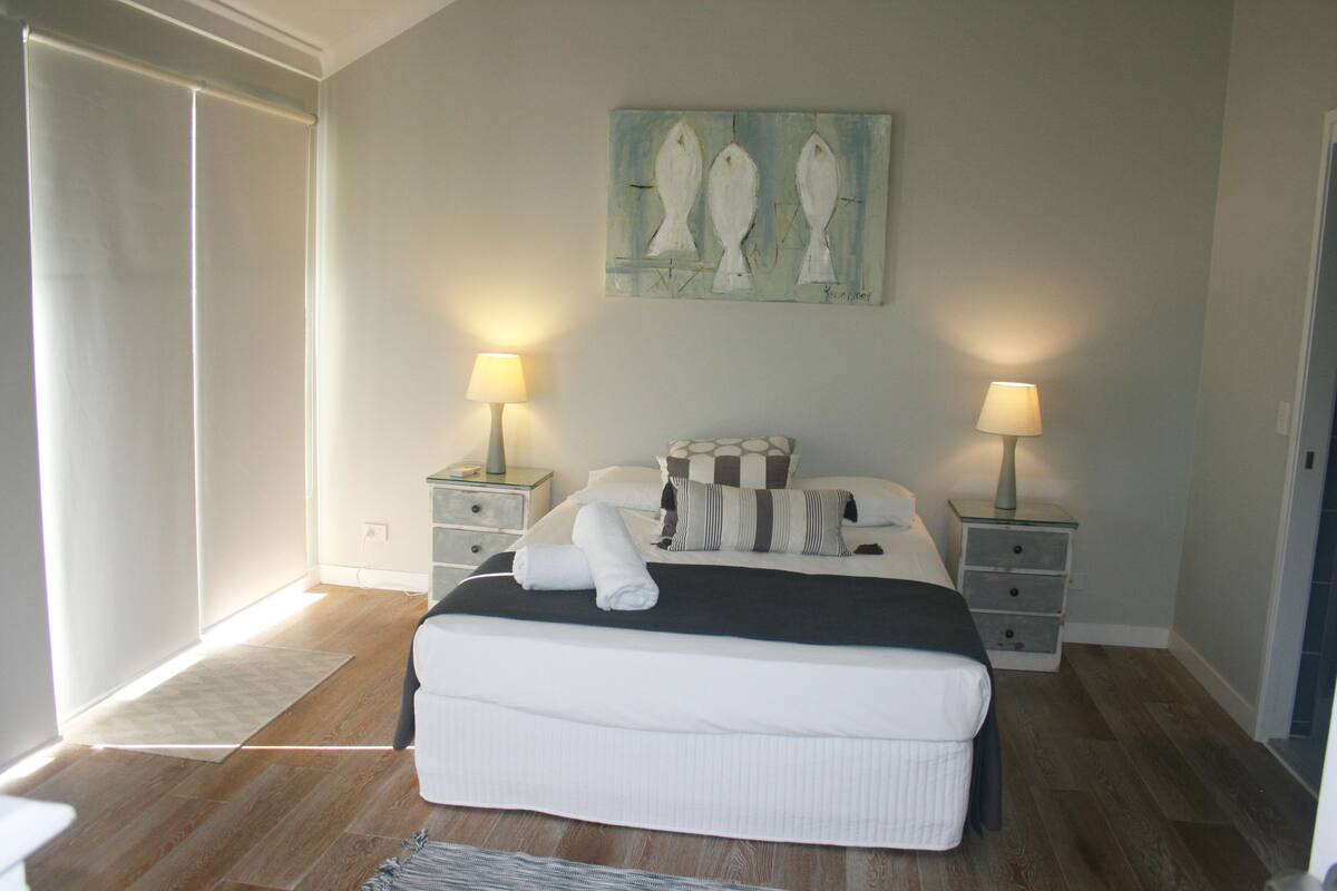 Une chambre à coucher avec un lit, deux tables de chevet avec des lampes, un tableau au mur et une fenêtre avec des rideaux.