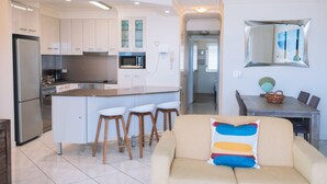 A modern kitchen with white cabinets, a built-in microwave, and a stainless steel refrigerator. There is a dining area with a wooden table and chairs. - Surfers Horizons Resort (Palm Beach)