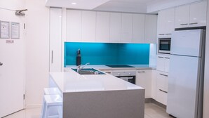 A modern kitchen with white cabinets, a blue backsplash, a stainless steel sink, and a built-in oven. - Surfers Horizons Resort (Palm Beach)