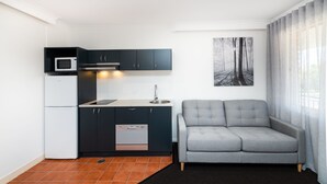 A compact living space with a kitchenette, grey sofa, and a painting of a forest. - River Motel (Queanbeyan East)