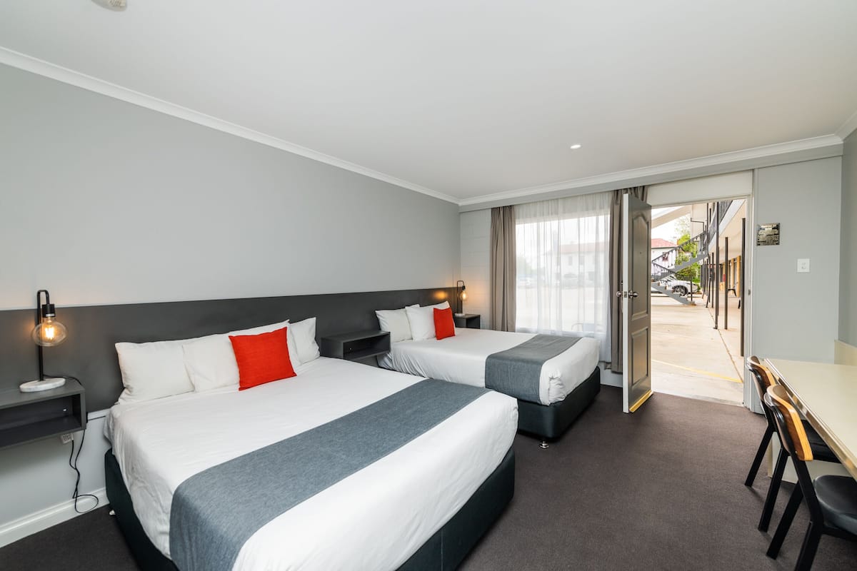 Habitación de hotel con dos camas, un escritorio y vista al exterior.
