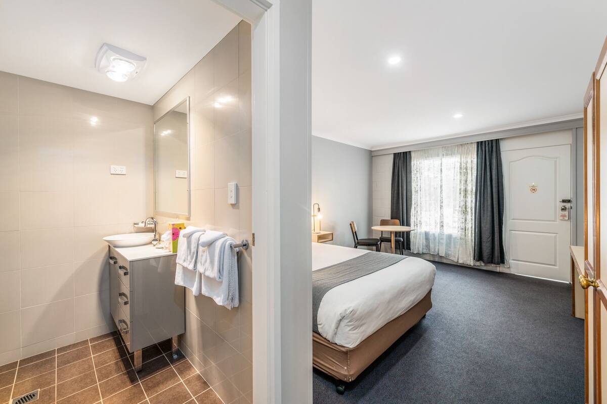 Habitación de hotel con baño, cama, escritorio y silla.