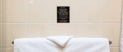 A white towel hanging on a metal towel rack in a bathroom with beige tiles. A sign above the towel explains the hotel's commitment to conserving water and provides instructions for towel reuse.
