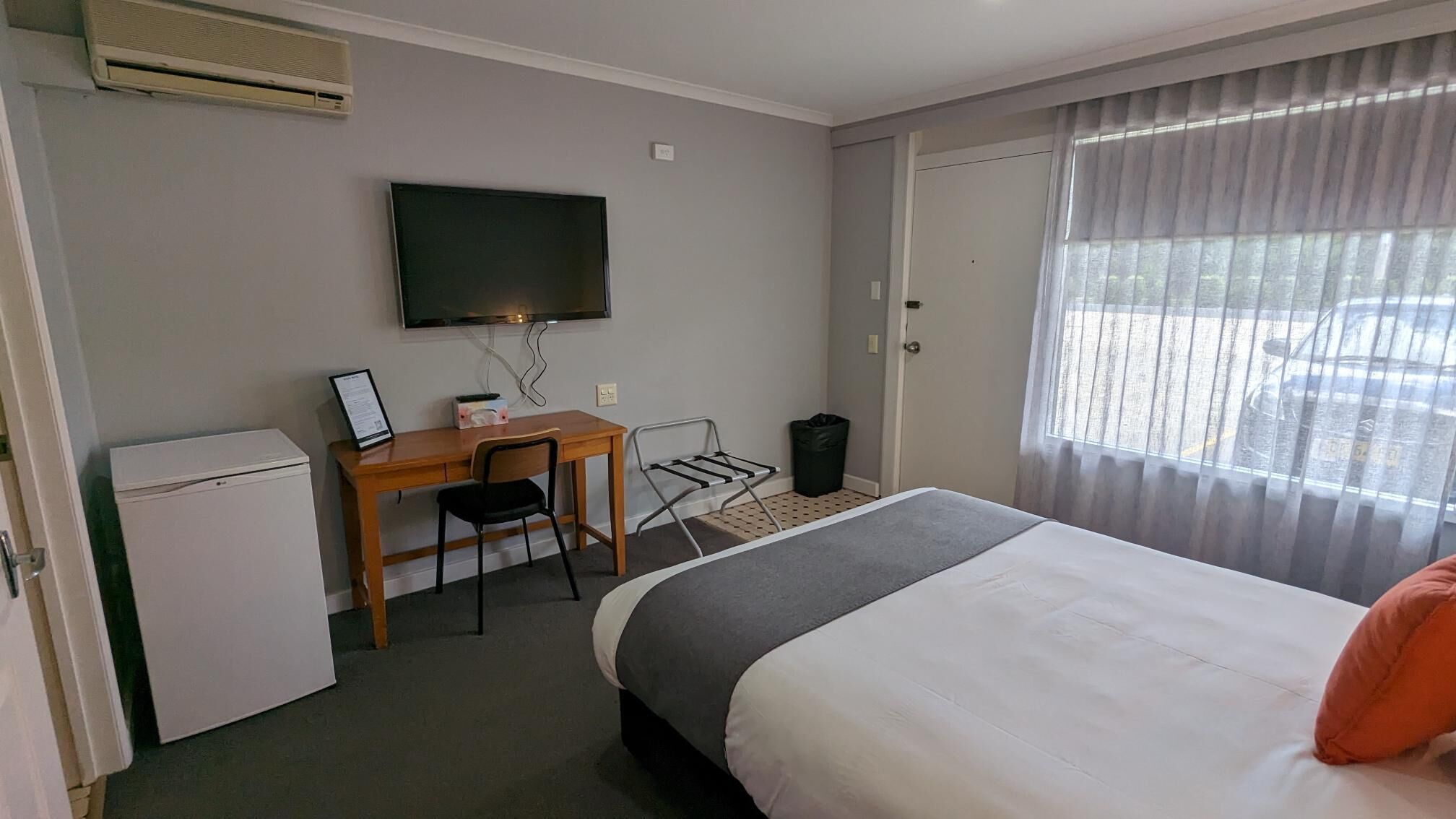 Habitación de hotel con una cama, un escritorio con silla, televisión y un refrigerador pequeño.