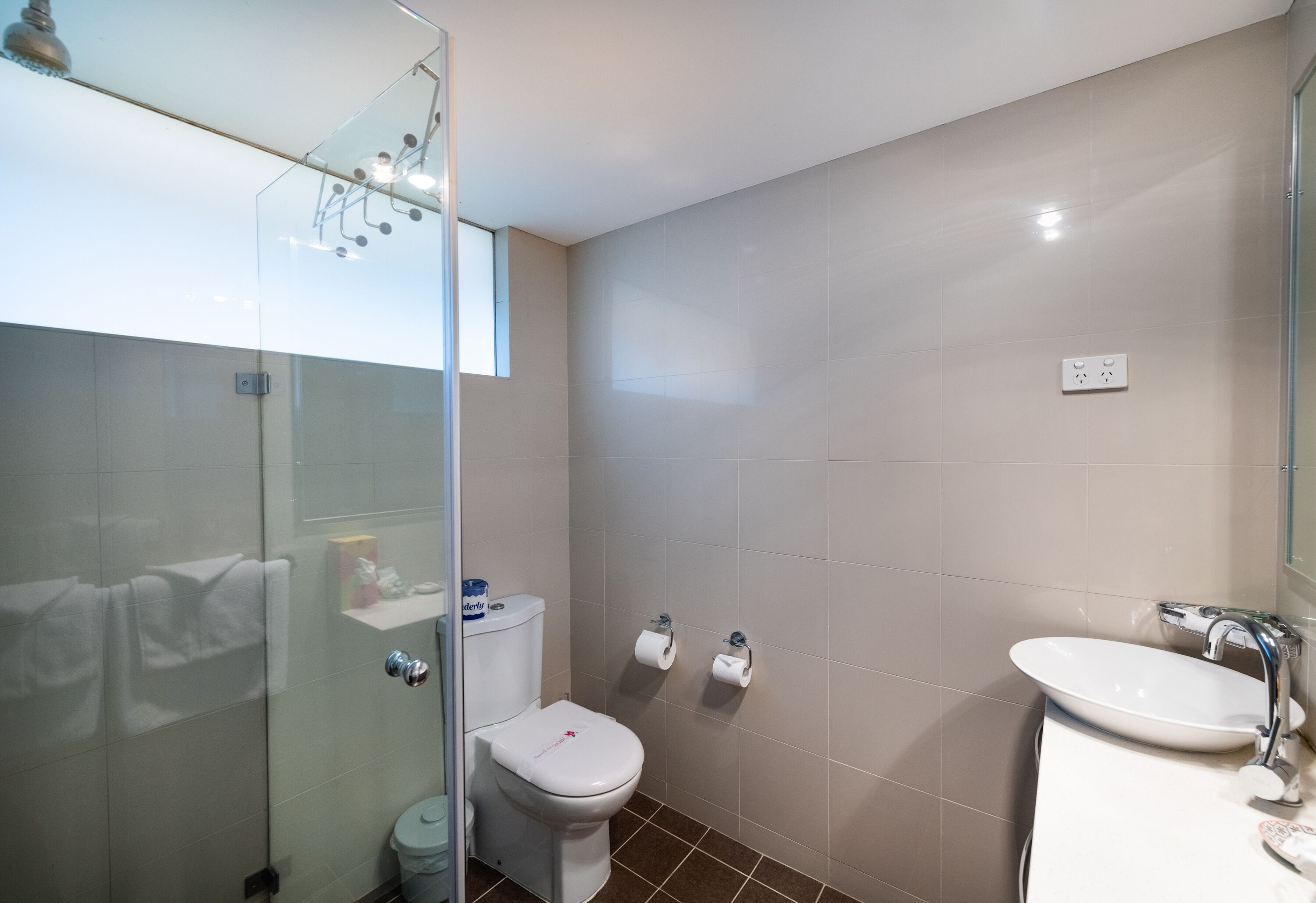 Une salle de bain moderne avec une douche à parois de verre, des toilettes blanches et un lavabo avec un miroir.