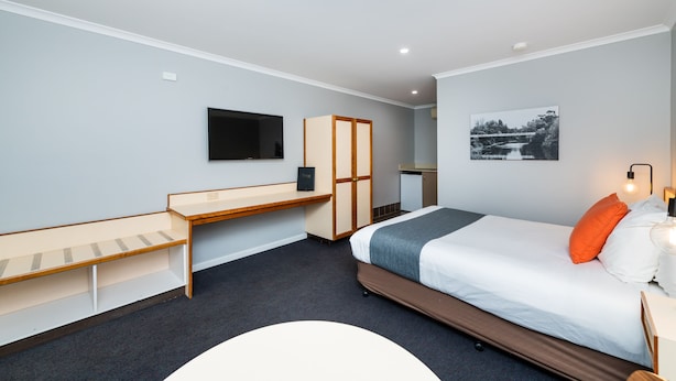 Ein Hotelzimmer mit Bett, Schreibtisch, Kleiderschrank, Fernseher und einem Bild an der Wand.