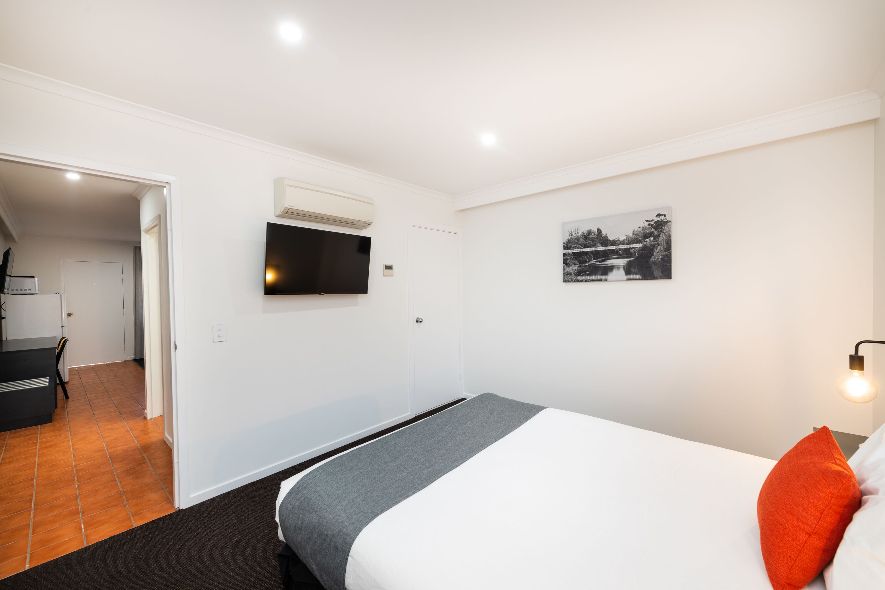 A modern hotel room with a bed, a flat-screen TV, a painting, and a small table.