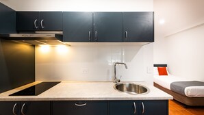 A compact kitchen with dark cabinets, a stainless steel sink, and a built-in induction cooktop. - River Motel (Queanbeyan East)