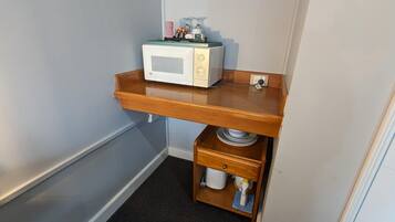 A compact kitchenette with a microwave, a wooden shelf, and a small drawer.