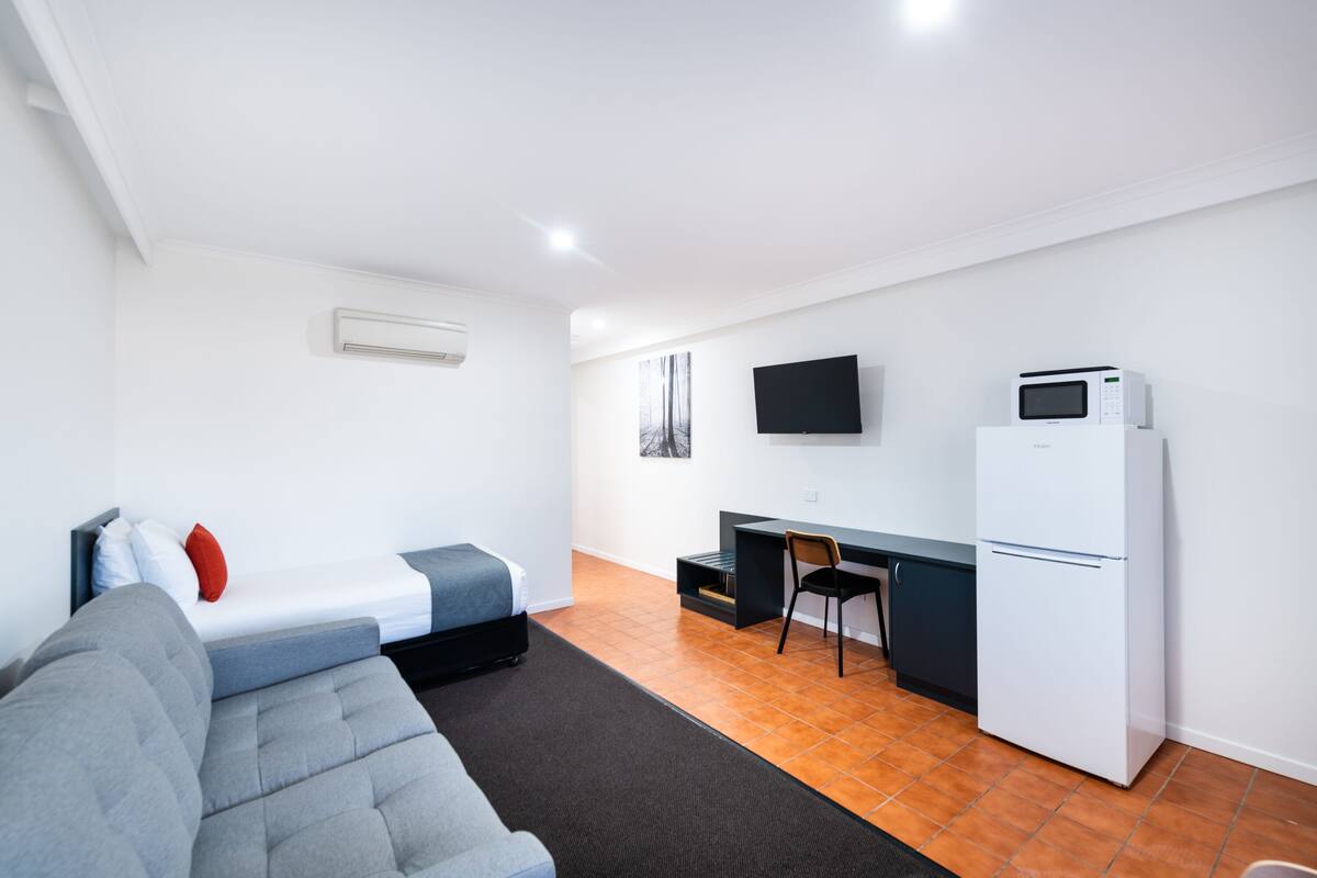 Un espacio habitable compacto con cama, sofá, escritorio, silla, televisor y refrigerador.