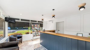 A reception area with a wooden counter, a seating area with leather chairs, a bulletin board with brochures, and a view of the outdoors through large windows. - River Motel (Queanbeyan East)