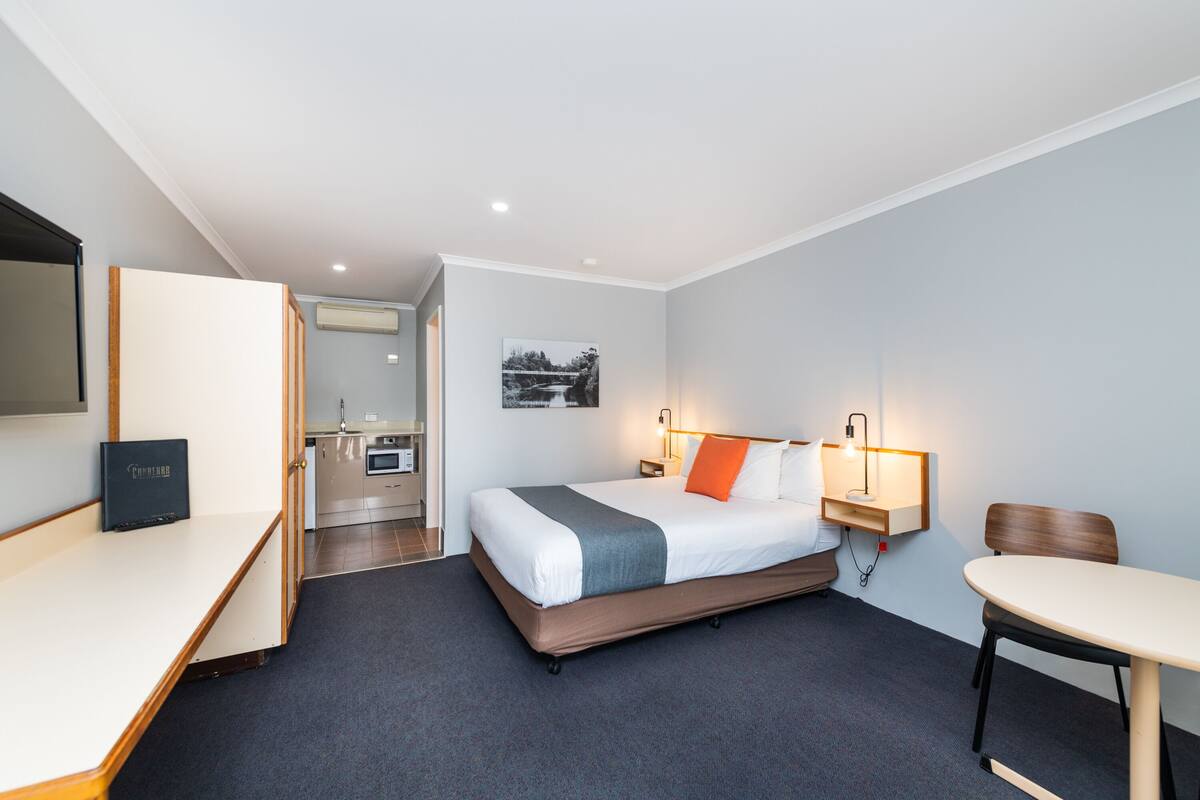Una habitación de hotel moderna con cama, escritorio, silla y kitchenette.