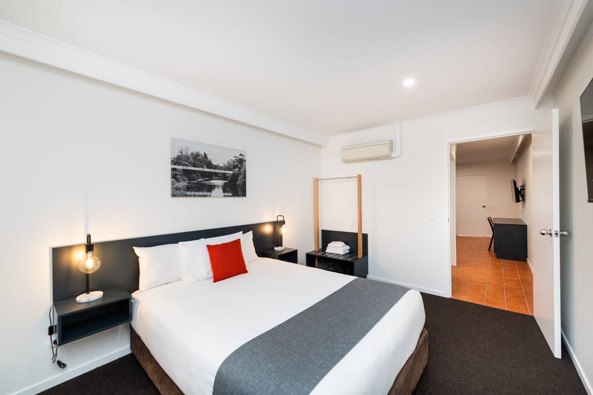 Una habitación de hotel moderna con una cama grande, mesitas de noche, un escritorio y una silla.