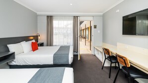 A hotel room with two beds, a desk, chairs, a TV, and a view of the street. - River Motel (Queanbeyan East)