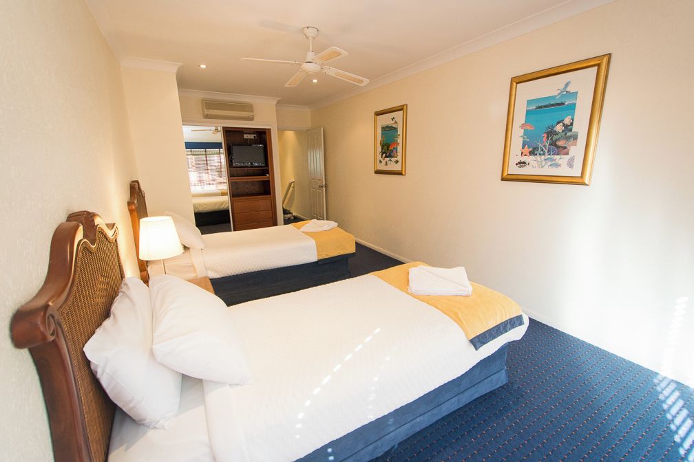 A hotel room with two beds, a ceiling fan, a large window, and artwork on the wall.