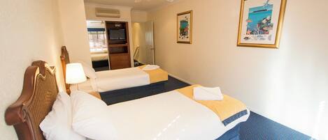 A hotel room with two beds, a ceiling fan, a large window, and artwork on the wall.