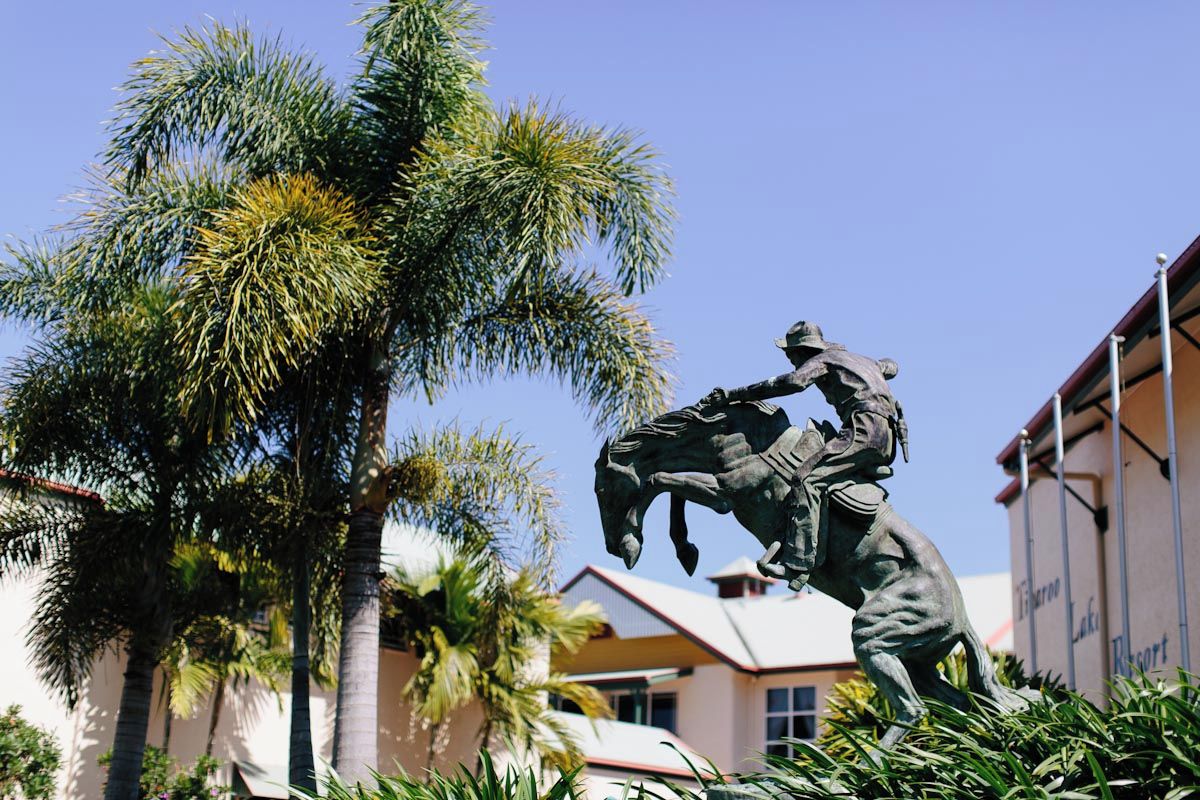 A statue of a man on horseback in a public square with palm trees and a building in the background.