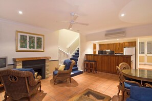 A living room with a fireplace, wicker furniture, a staircase, and a kitchen area with wooden cabinets. - Tinaroo Lake Resort (Tinaroo)