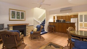 A living room with a fireplace, wicker furniture, a dining table, and a kitchen area with wooden cabinets and a refrigerator. - Tinaroo Lake Resort (Tinaroo)