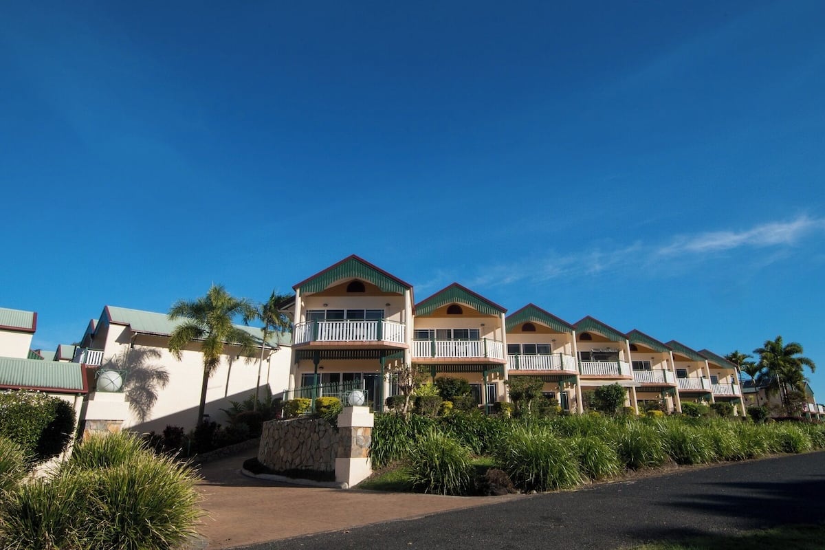 Une rangée de bâtiments d’hôtels situés en bord de mer, dotés de balcons, d’un mur de soutènement en pierre et d’un aménagement paysager de style tropical.