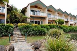 Un hotel de varios pisos con balcones, una escalera de piedra y jardines bien cuidados.