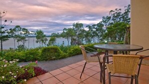 A patio with a round table and wicker chairs overlooking a body of water, surrounded by greenery. - Tinaroo Lake Resort (Tinaroo)