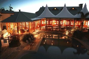 Un hotel con piscina, mobiliario exterior y una zona de comedor cubierta.