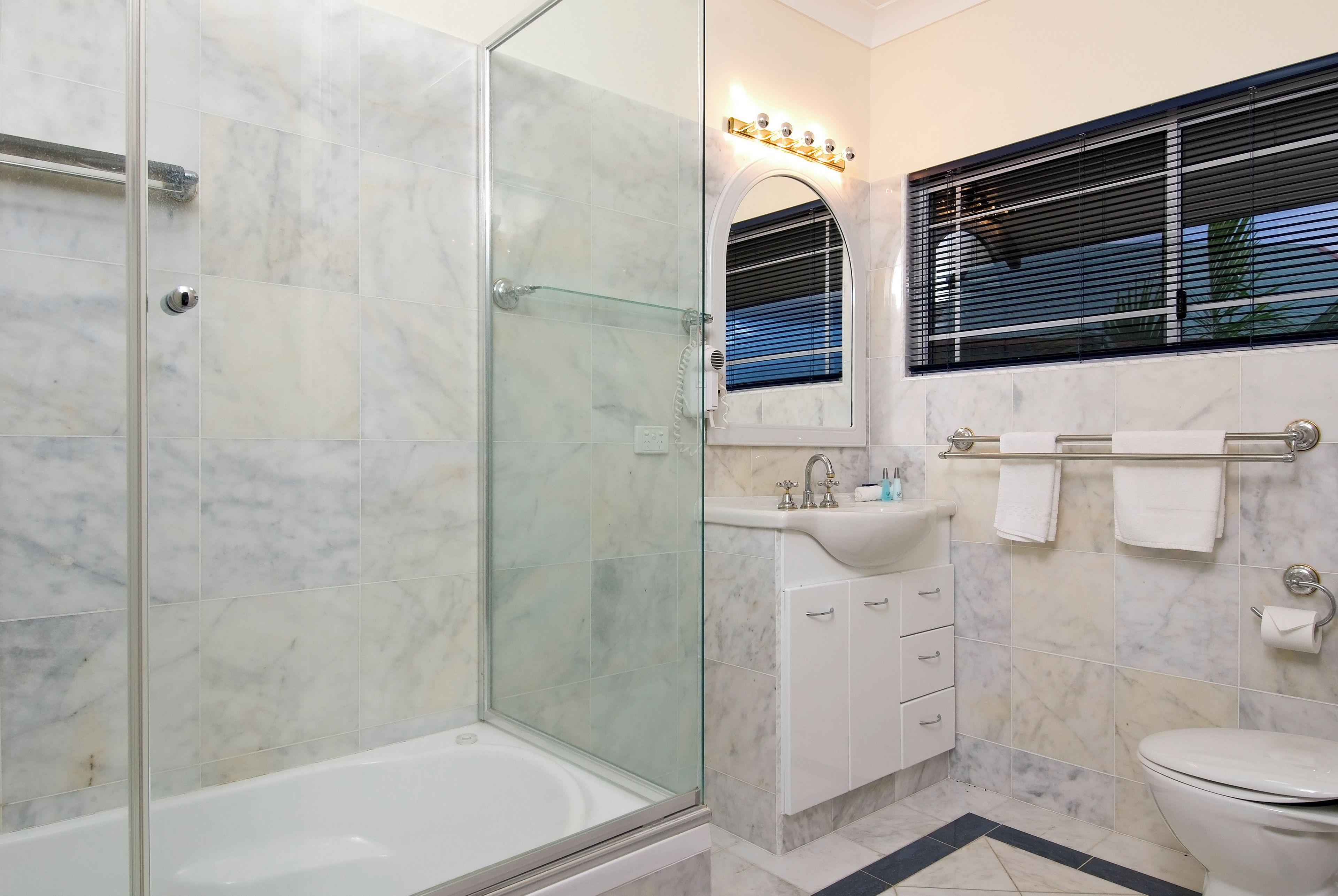 A bathroom with a glass-enclosed shower, a white bathtub, a sink with a mirror, and a toilet.