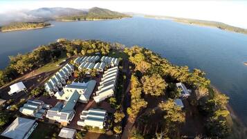 An aerial view of a lakeside resort with multiple bungalow-style accommodations, a dock, and a small island with a boat.