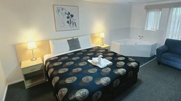 Ein Hotelzimmer mit einem Bett, Nachttischlampen, einem blauen Sofa, einer Badewanne und einem gerahmten Kunstwerk an der Wand.