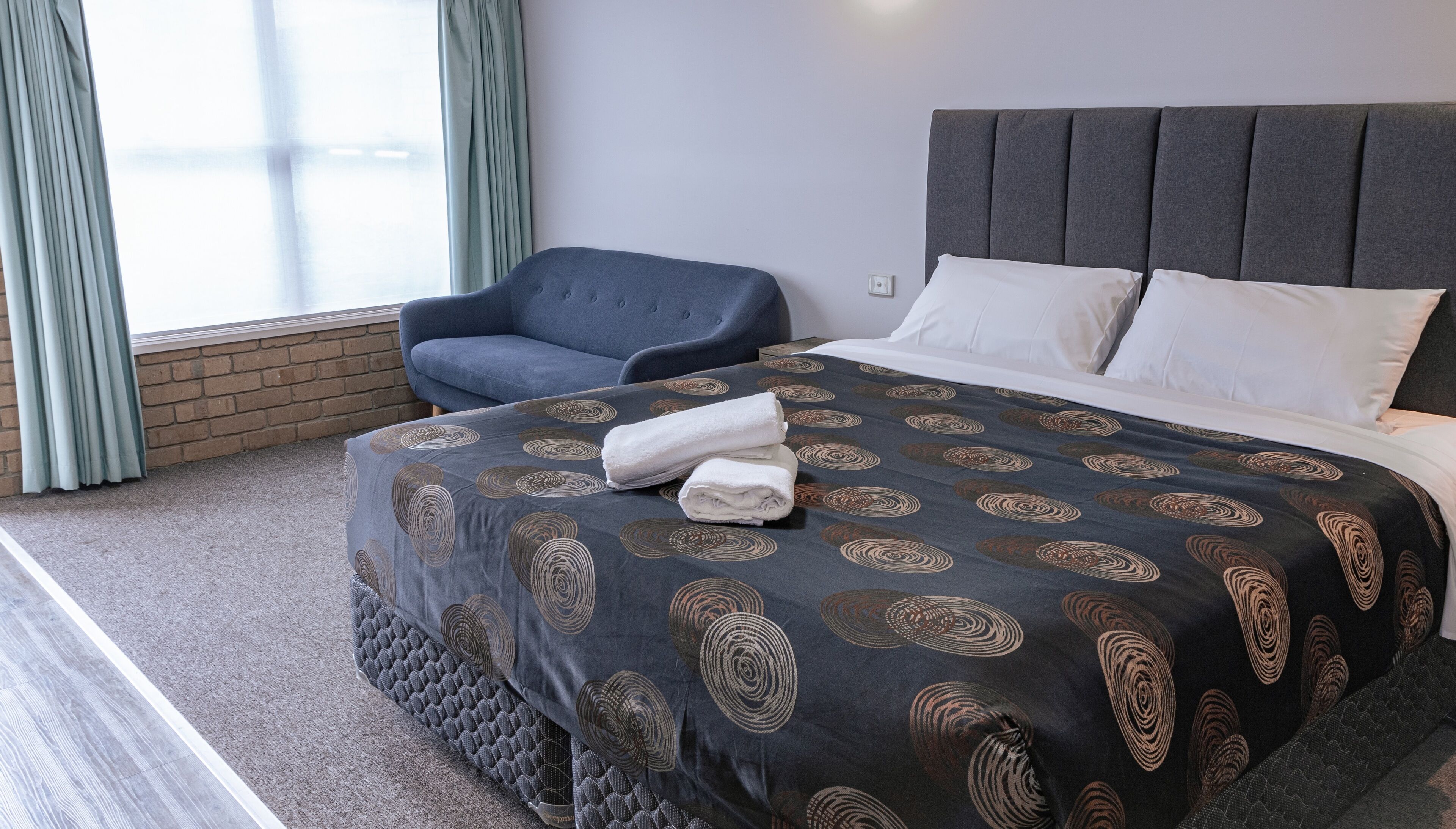A hotel room with a bed, a chair, and a window with curtains.