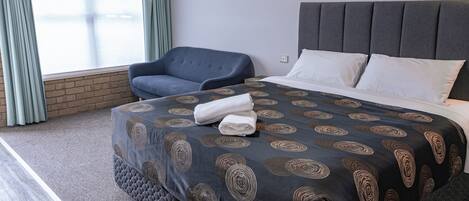 Ett hotellrum med en säng, en stol och ett fönster med gardiner.