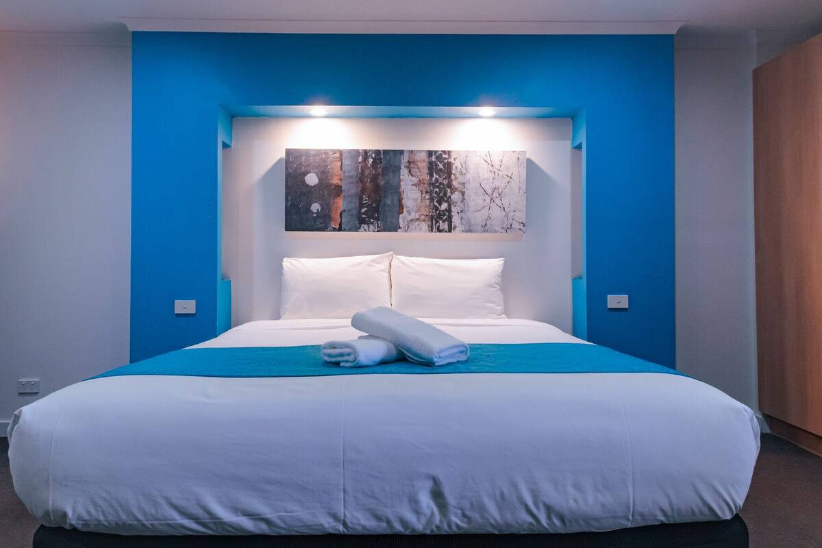 Un dormitorio moderno con una cama grande, paredes azules de acento, un armario de madera y un cuadro sobre la cama.