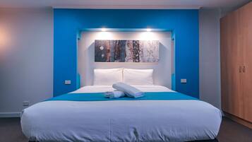 A modern bedroom with a large bed, blue accent walls, a wooden wardrobe, and a painting above the bed.