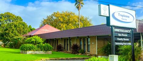 A Tropicana Motor Inn with a red roof, a signboard indicating free Wi-Fi, and a list of amenities including spa rooms, family rooms, and a swimming pool & BBQ.