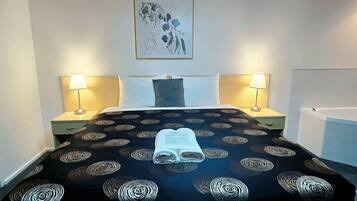 Hotelkamer met een bed, twee bedlampen, een hoofdeinde, een kunstwerk in een lijst en een badkamer met een bad.