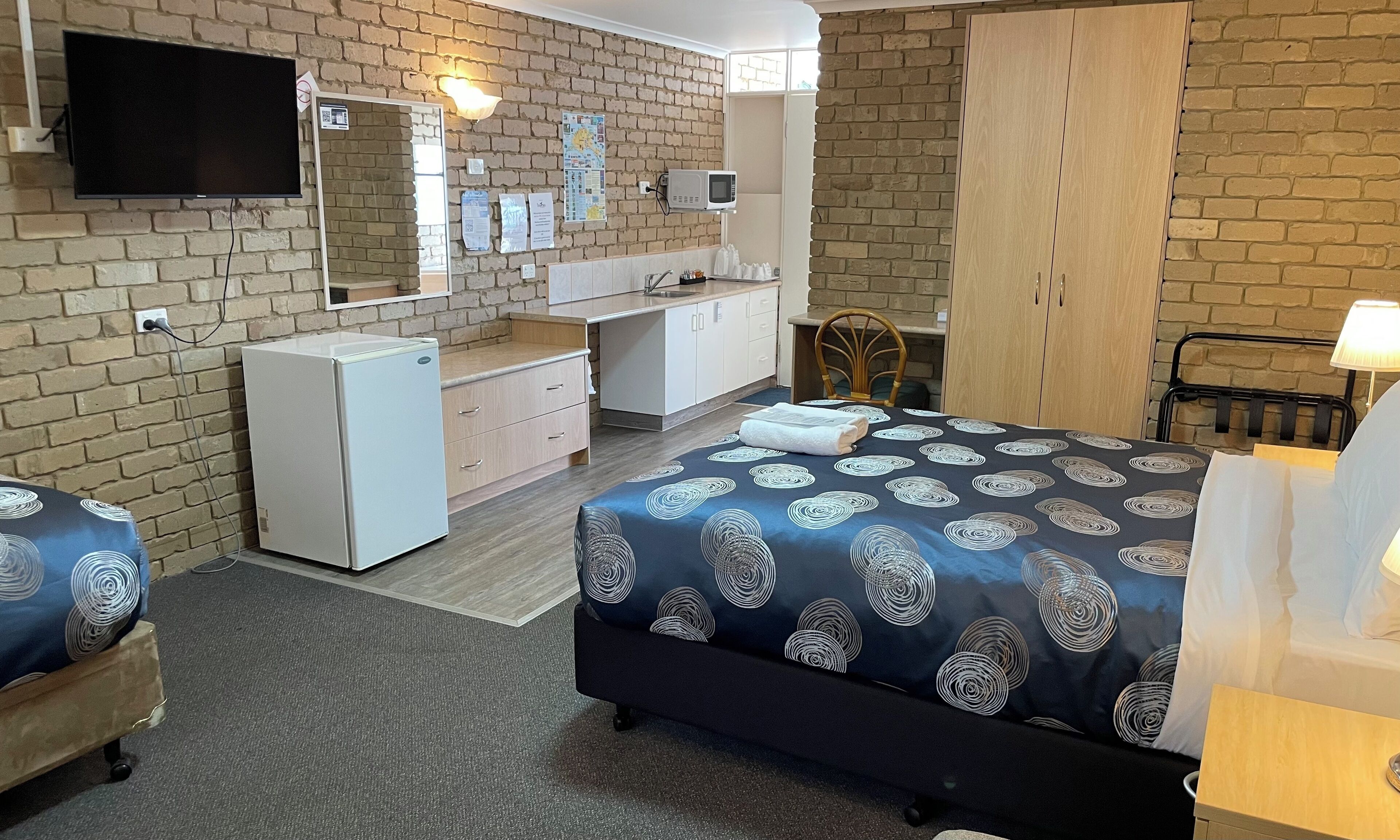 Una habitación de hotel con kitchenette, una cama con colcha estampada, televisor y un espejo grande.