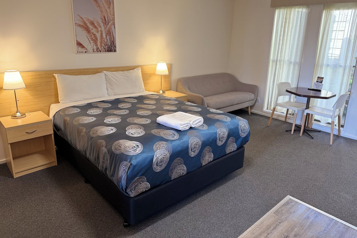 Habitación de hotel con cama, dos lámparas de noche, escritorio con silla, sofá y ventana con cortinas.
