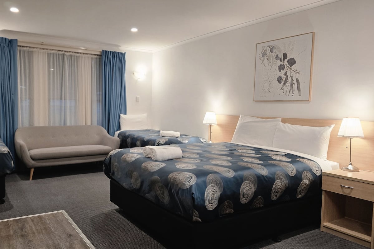 Una habitación de hotel con cama, dos mesitas de noche, un escritorio, una silla y un sofá.