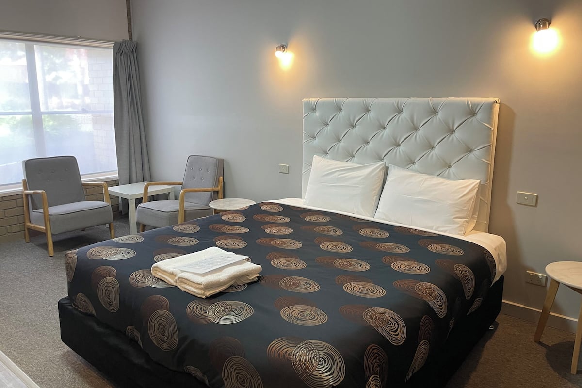 Habitación de hotel con una cama grande, dos sillas, una mesita y una ventana con cortinas.