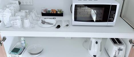A kitchenette with a microwave, toaster, kettle, and various utensils and dishes.