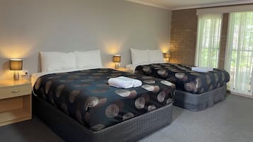 Une chambre d’hôtel avec deux lits, chacun recouvert d’une couvre-lit à motifs, dotée de lampes de chevet et d’une fenêtre ornée de rideaux légers.