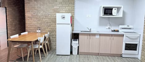 Cocina compacta con refrigerador, microondas, lavaplatos y estufa. Hay una mesa de madera con sillas.
