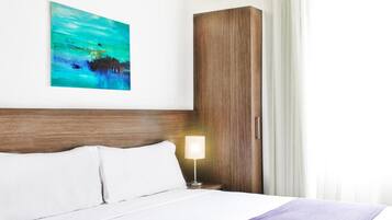 Una habitación de hotel con cama, mesita de noche, lámpara, armario y un cuadro en la pared.