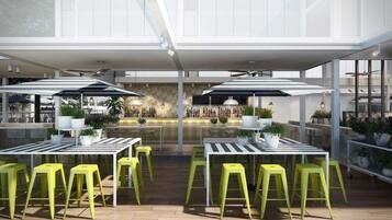 An outdoor dining area with tables and yellow chairs, a bar with bottles, and potted plants.