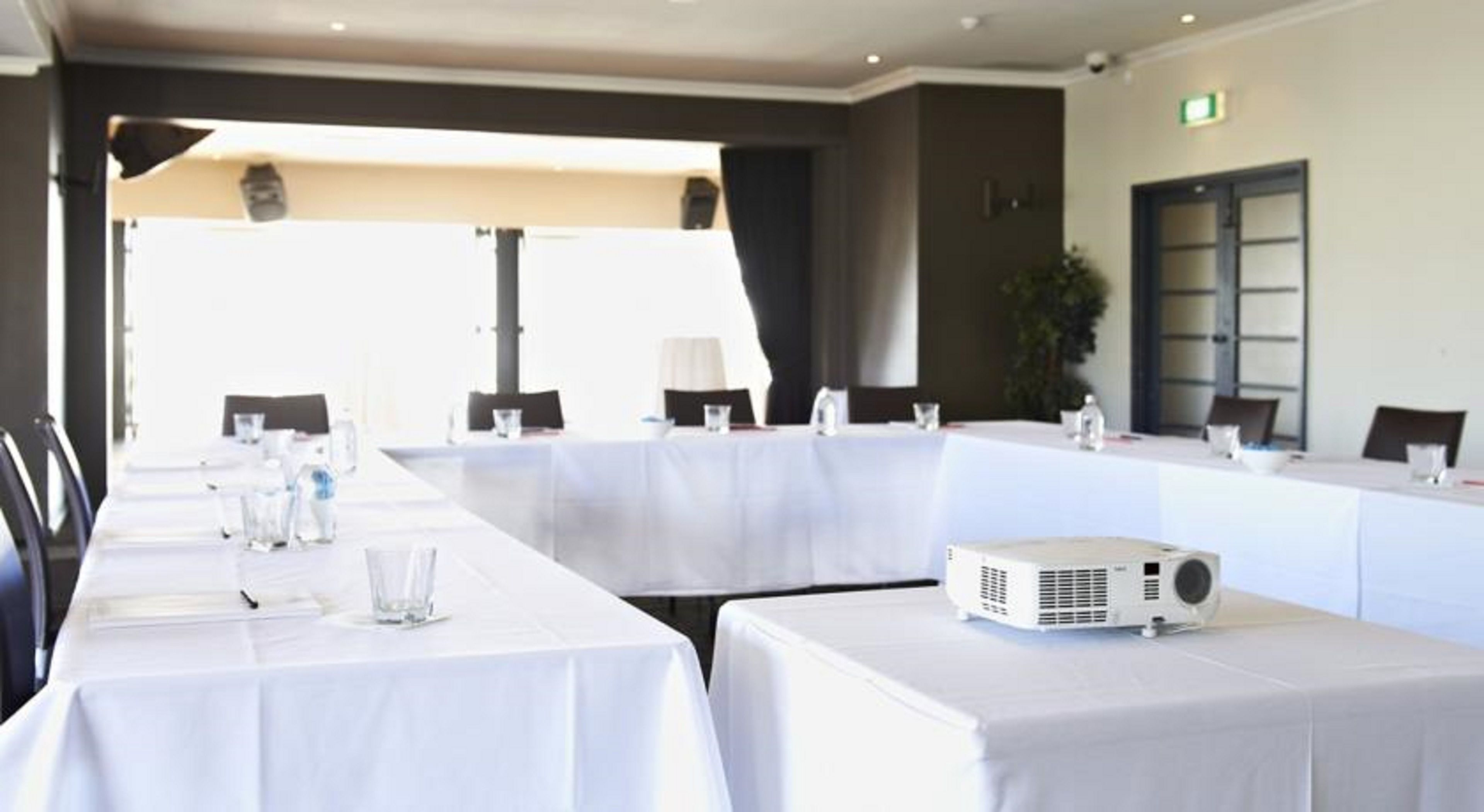 A conference room with long tables, chairs, a projector, and a plant.